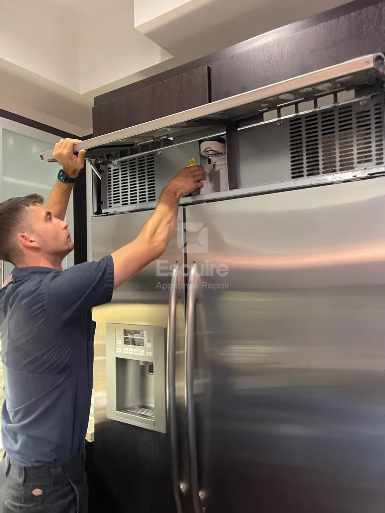 Technician servicing the top condenser area of a built-in stainless refrigerator